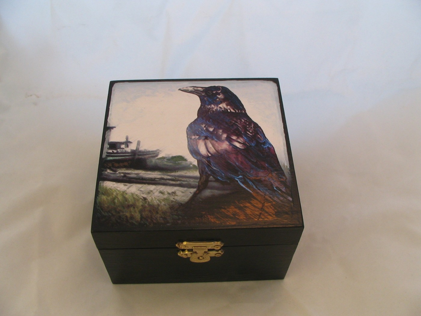 Small black hinged box, the lid painted with an iridescent crow standing on a shoreline log with a beached skiff behind