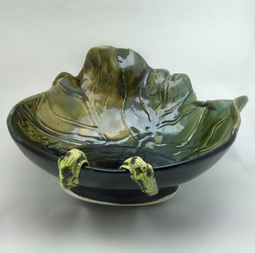 A large hand-built bowl formed as a lettuce leaf, glazed deep green over black, with two yellow clay slugs climbing the rim