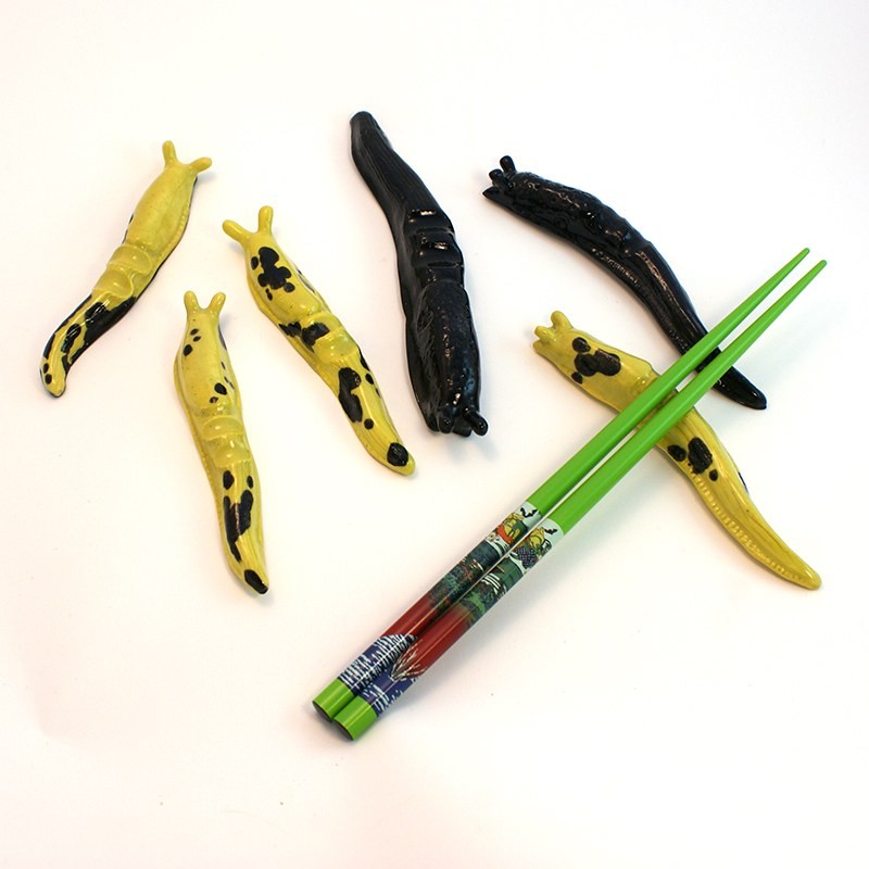 Six clay banana slugs used as chopstick rests, four yellow with black spots and two glossy black, with a pair of green chopsticks