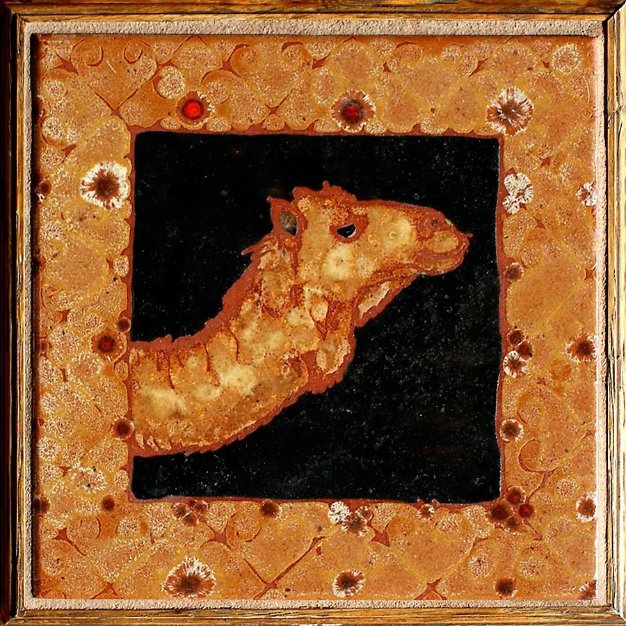 Square ceramic tile in a wooden frame, a camel's head and neck in rust and cream against a black ground, surrounded by a patterned floral border