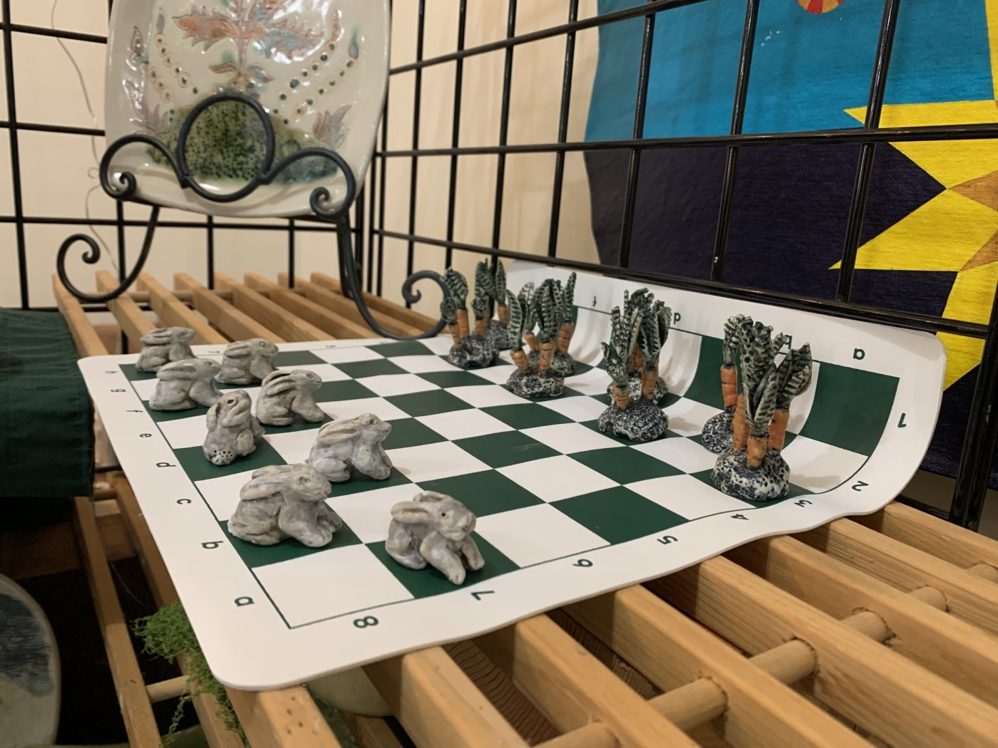 A chess set of small clay figures on a board — pale rabbits facing ranks of carrots with green tops