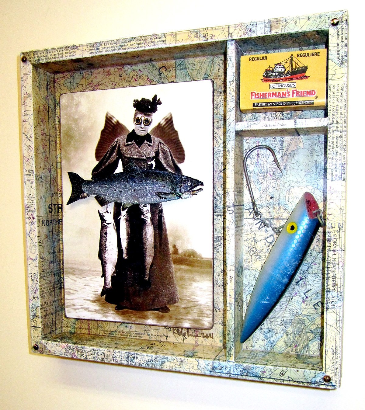 Assemblage on a chart-papered panel: a sepia photograph of a winged woman in Victorian dress holding a large salmon, with a Fisherman's Friend lozenge tin and a blue fishing lure mounted beside it